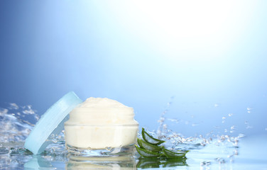 Opened jar of cream in water splashes on blue background