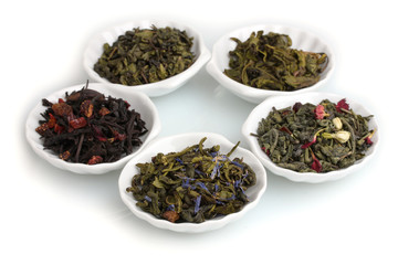 Green and black dry tea leaves in plates isolated on white