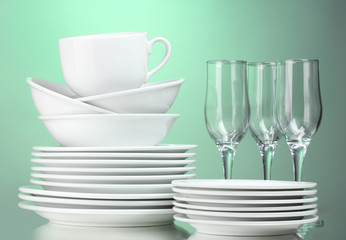 Clean plates, cups and glasses on green background