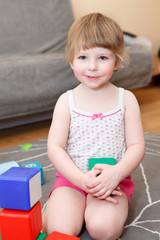 Portrait of small girl playing with color bricks on floor