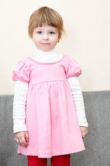 Portrait of small girl in pink dress standing on couch