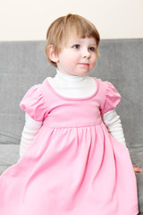 Portrait of small girl in pink dress sitting on couch