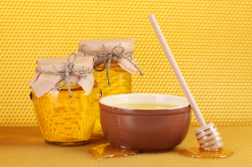 Jars of honey, bowl and wooden drizzler with honey