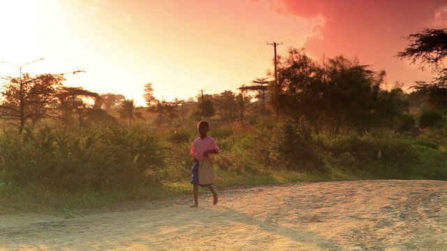 Small boy walking along a dirt road at sunrise in Africa.