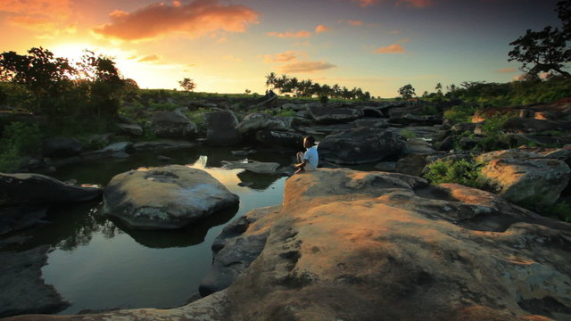 Child sitting on a rock near a village in Kenya at sunset.
