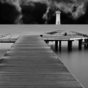 Long exposure on wooden pier at dawn with lighthouse and storm c
