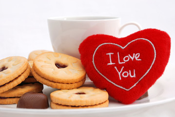 Plush heart and cookies on the white plate near to white cup