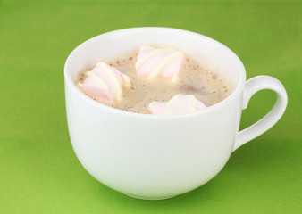 Cup of cappucino with marshmallows on green background