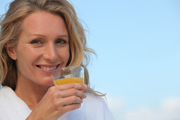 Closeup of a woman in a bathrobe drinking orange juice outdoors
