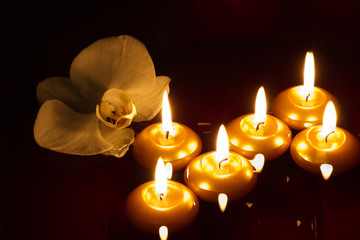 Floating candles and orchid blossom in dark. Spa, relaxation and wellbeing concept