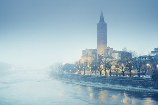 Sant'Anastasia church and Adige River at a foggy winter evening.