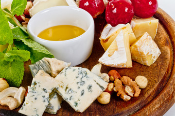 Various types of cheese with honey, nuts and grapes on plate, is