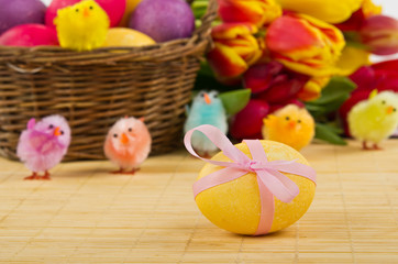 Yellow egg with ester basket and tulips on background