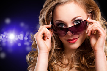 junge blonde Frau mit Sonnenbrille vor Lichterhintergrund