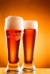 Two glasses with cold beer over yellow background