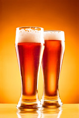 Two glasses with cold beer over yellow background