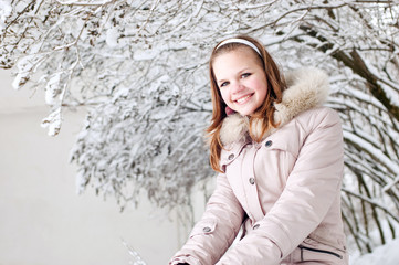 Beautiful young girl sits on to snow in warm clothes in winter o