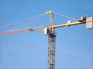 Yellow construction hoisting crane over blue sky