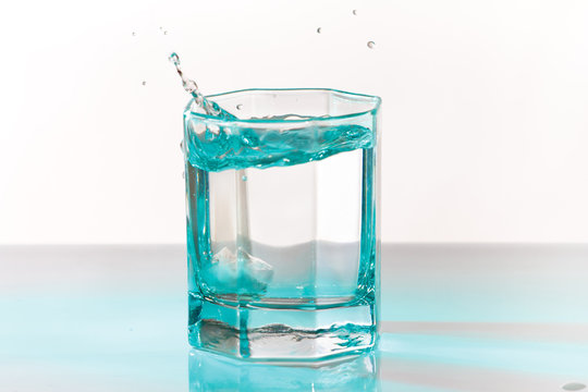 Glass of fresh ice water with splash in a turquoise light