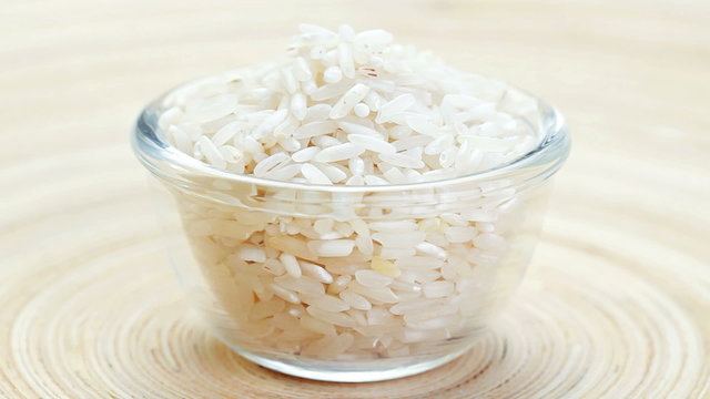 Polished long rice heap in a glass bowl rotating on wooden plate