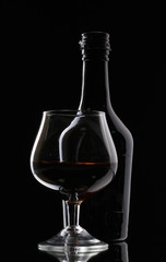 Glass of brandy and bottle on black background