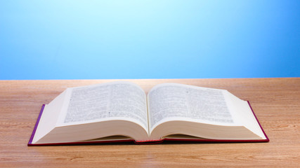 Open book on wooden table on blue background