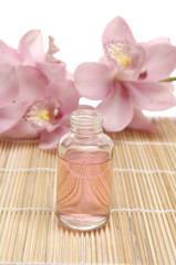 Two pink orchid and bottles with essential oil on bamboo mat