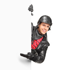 A smiling motorcycler gesturing welcome behind a white panel