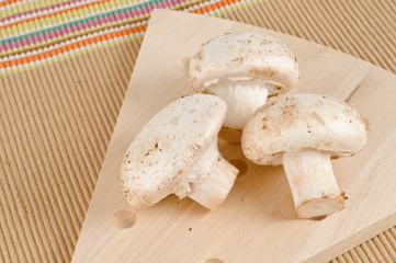 A wood cutting board with three white mushrooms