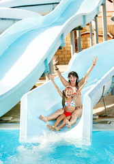 Child with mother on water slide at aquapark.