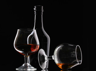 Glasses of brandy and bottle on black background
