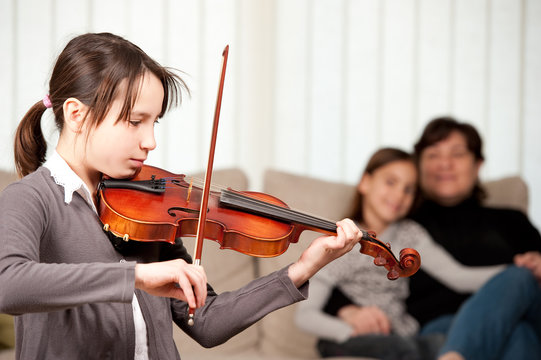 Young Girl Playing Violin With Her Family At Home