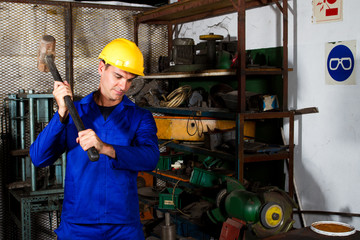 factory blue collar worker using big hammer in workshop