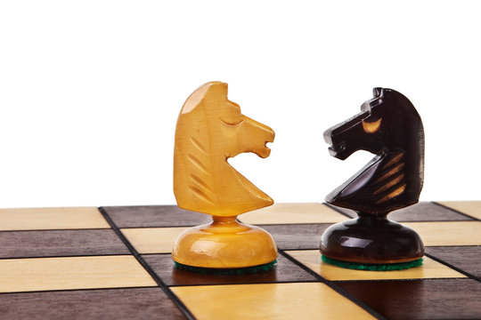 Two chess knight figures on chessboard over white background.