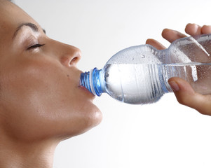 Mujer bebiendo agua mineral de una botella plástica.