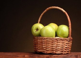 juicy green apples in basket on wooden table on brown background