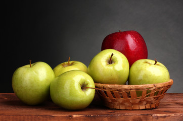 juicy sweet apples in basket on wooden table on gray background