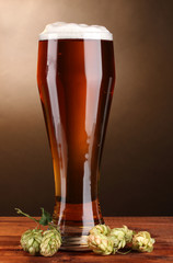 beer in glass and green hop on wooden table on brown background
