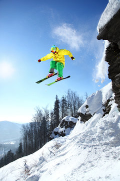 Cool skier jumping against blue sky from the rock