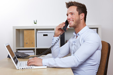Lachender Mann im Büro am Telefon