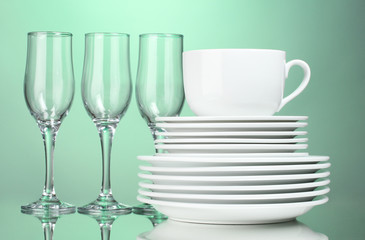 Clean plates, cup and glasses on green background