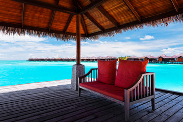 Sofa with red pillows on jetty in tropical lagoon