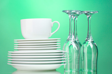 Clean plates, cup and glasses on green background