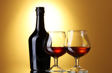 Glasses of brandy and bottle on yellow background