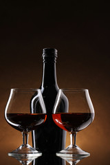 Glasses of brandy and bottle on brown background