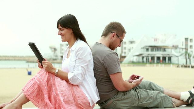 Happy young couple with tablet and cellphone on the beach