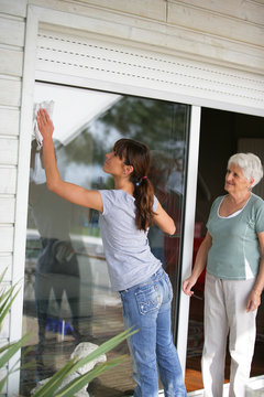 Woman cleaning a glass patio door for an elderly lady