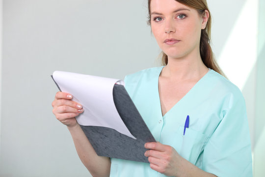 Nurse in hospital scrubs examining a clipboard
