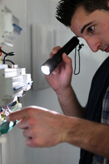 Electrician shining a torch on a fusebox