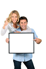 Excited couple pointing to a blank sign